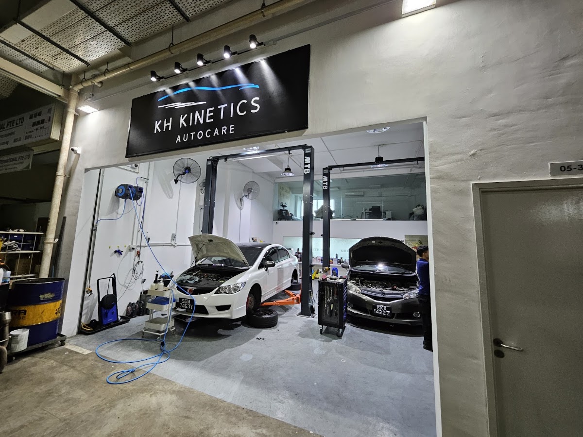 The KH Kinetics Autocare workshop at night, signboard lit, two cars in the bays with bonnets up